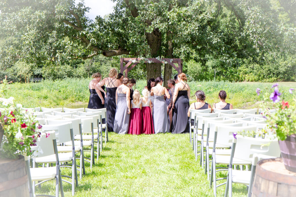 Bridal party gathered for pictures under the giant old oak tree with pond in the background at Pleasant Pastures Weddings and Events in Central Minnesota